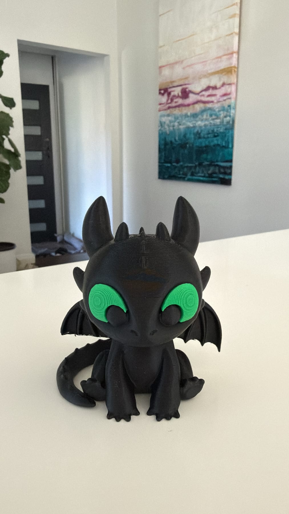 Black 3D-printed baby dragon with big green eyes