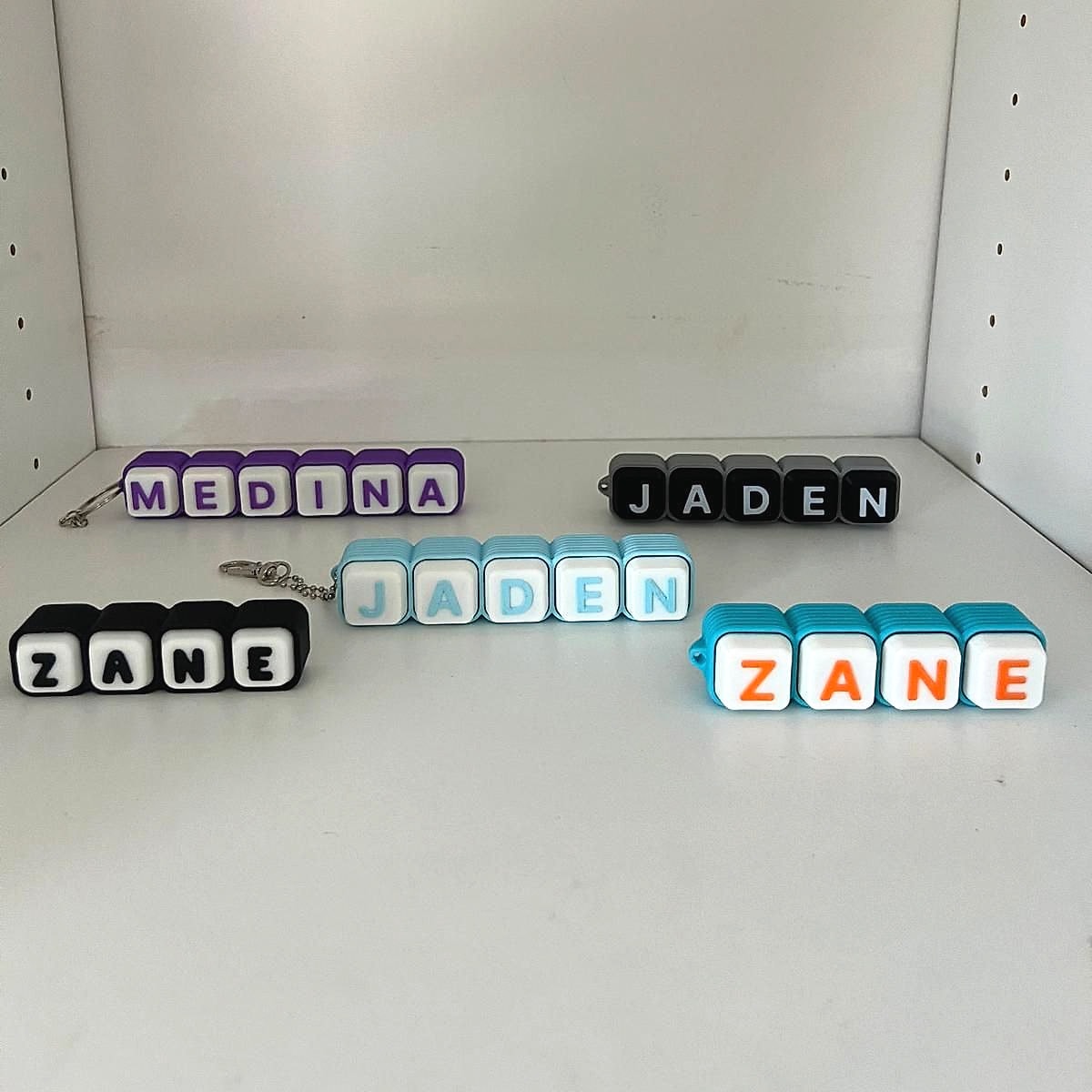 Five personalised name keychains made of letter blocks in purple, black, light blue and bright blue, spelling Medina, Jaden and Zane