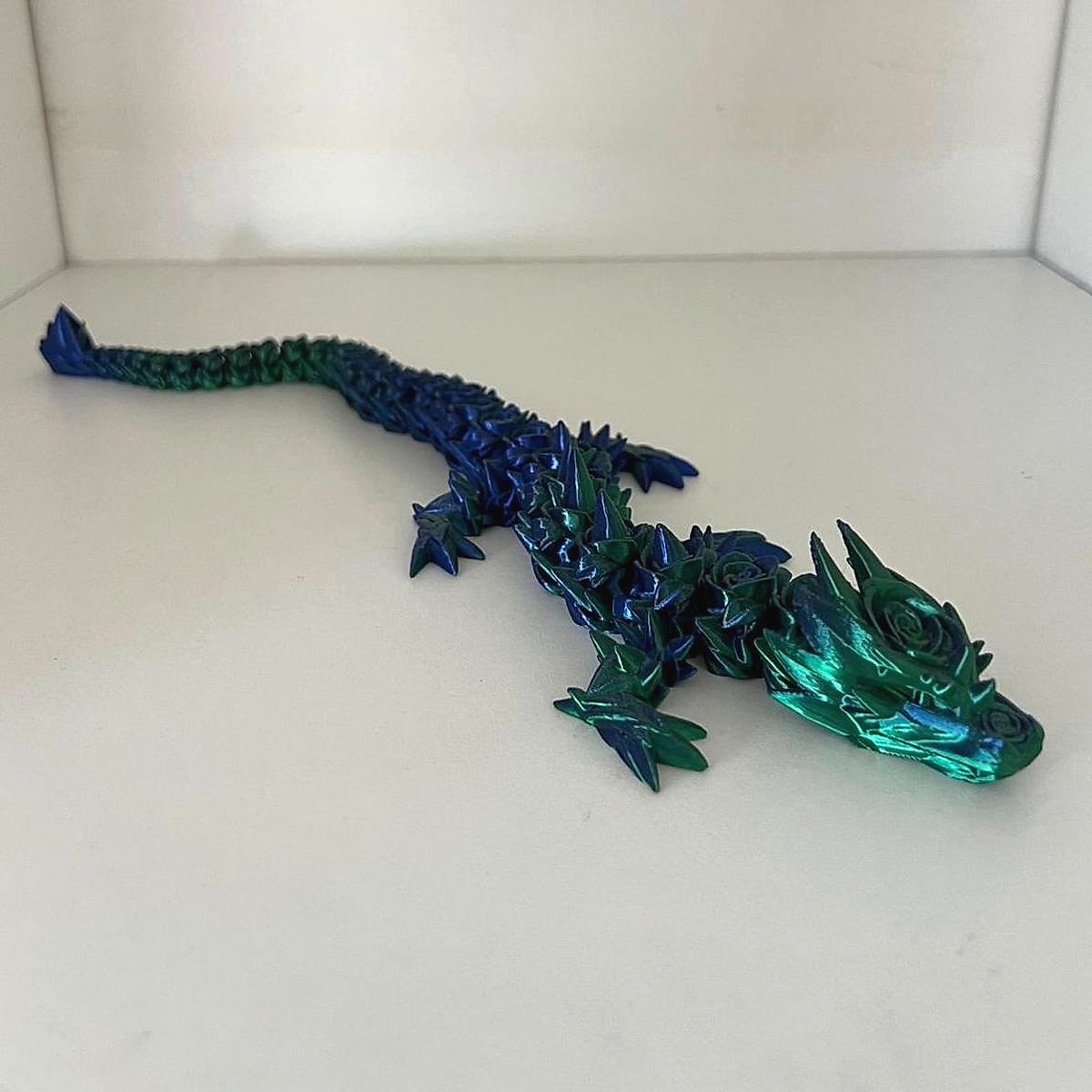 A long blue and green articulated dragon with roses on its head, resting on a white shelf